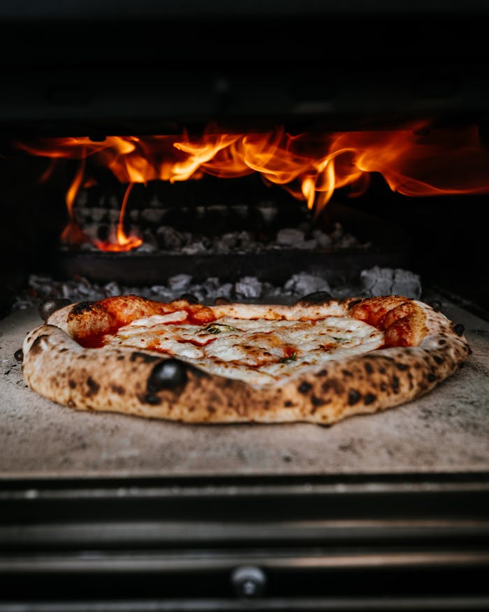 Close-up of authentic pizza cooking in a wood-fired oven with flames.